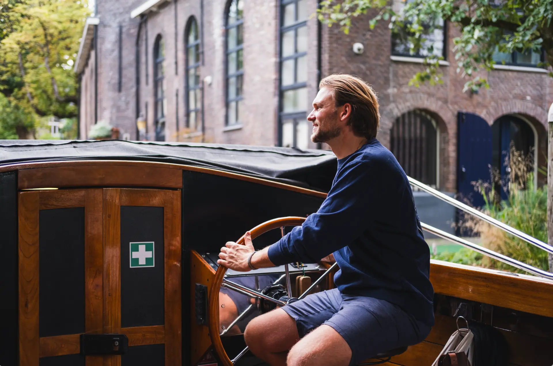 Schipper Daan aan het houten stuurwiel van de sloep langs een Utrechts pakhuis