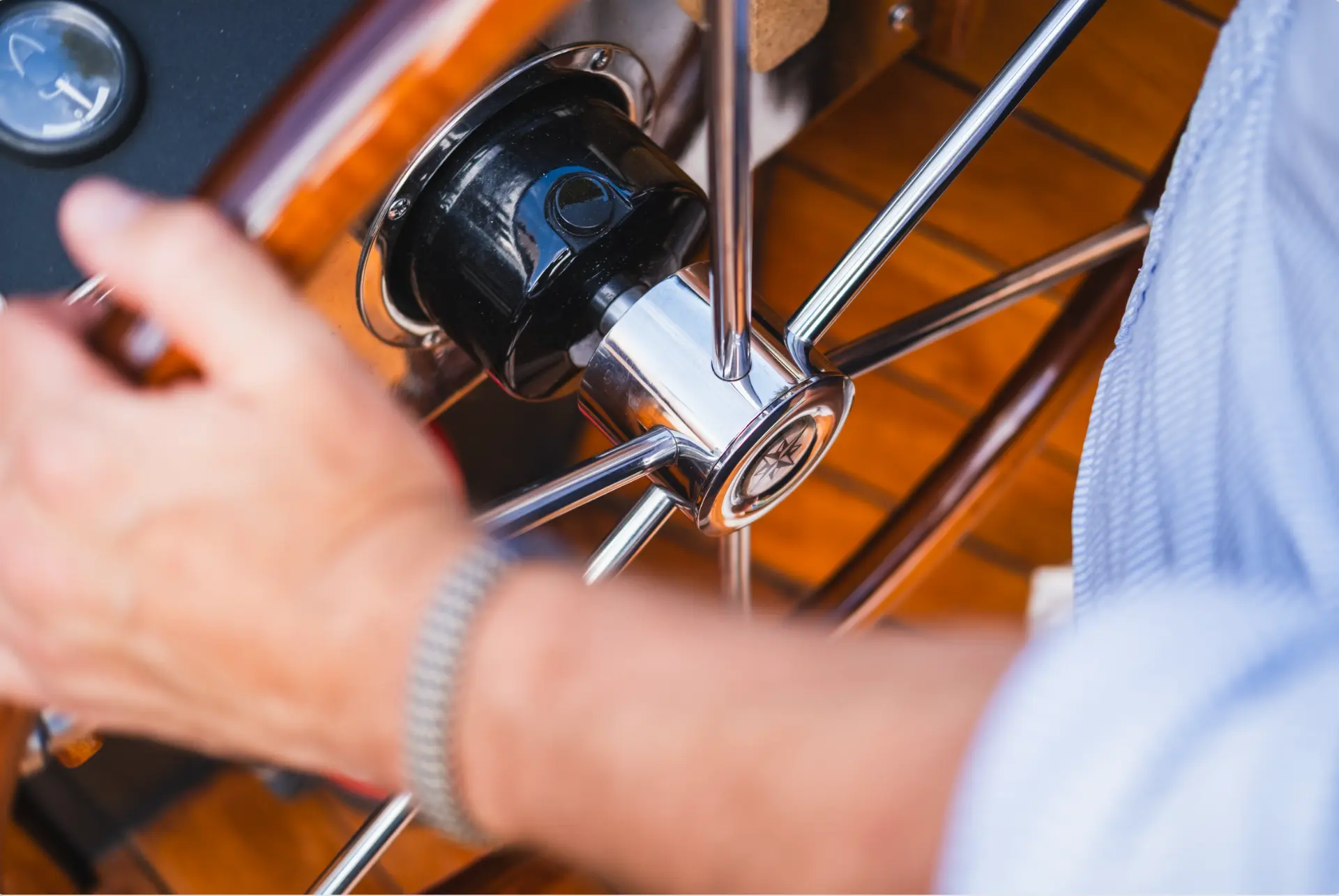 Detail van het chromen stuurwiel en teakdek van de boot met de hand van de schipper
