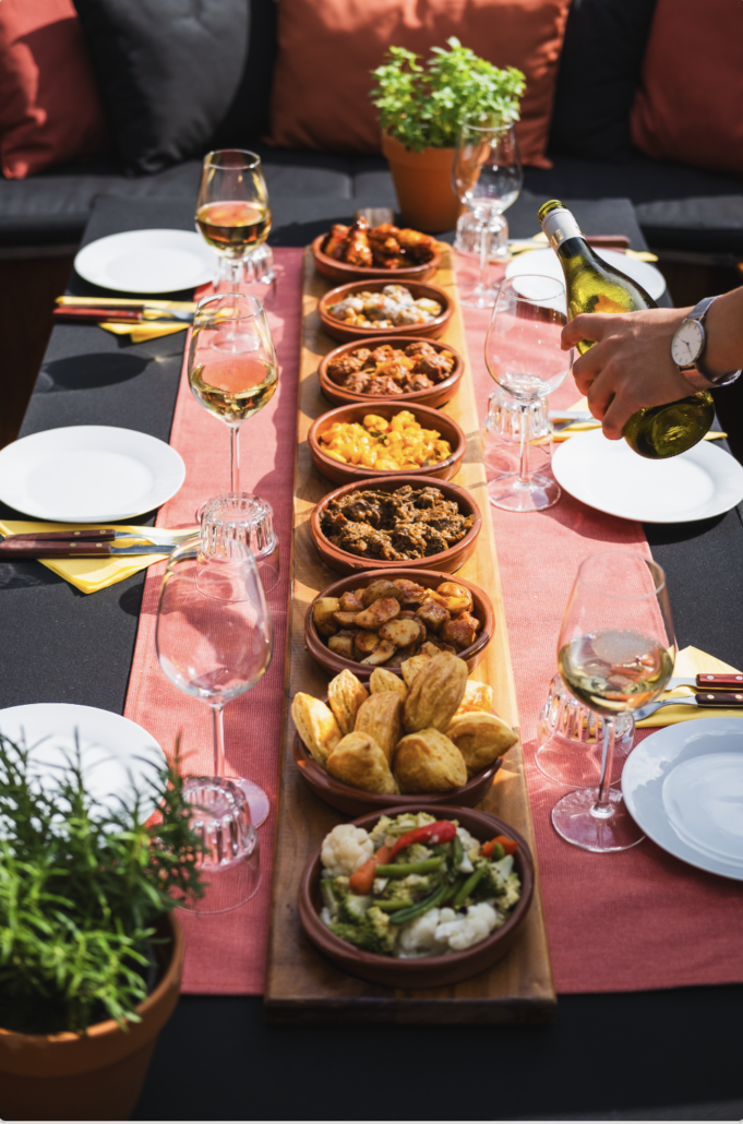 Gastvrouw schenkt witte wijn bij een lange tafel vol tapas aan boord van de sloep